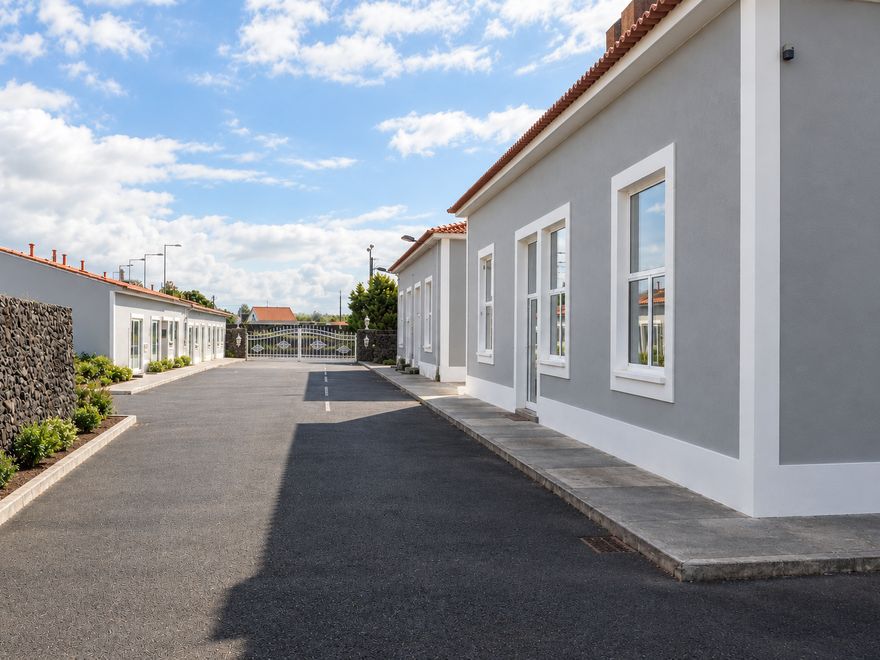 Caminho interior asfaltado entre as casas, com muros de pedra vulcânica