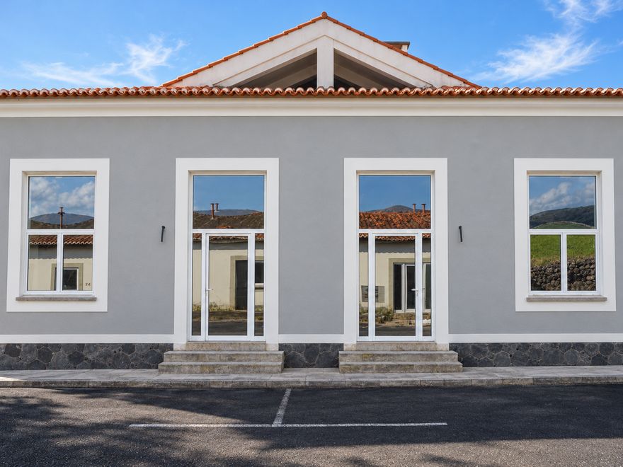 Fachada cinzenta com molduras brancas, portas envidraçadas e telhado de telha