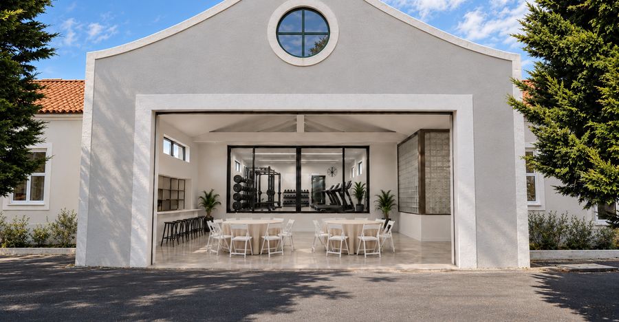 Pavilhão branco com mesas de convívio à frente e ginásio envidraçado ao fundo