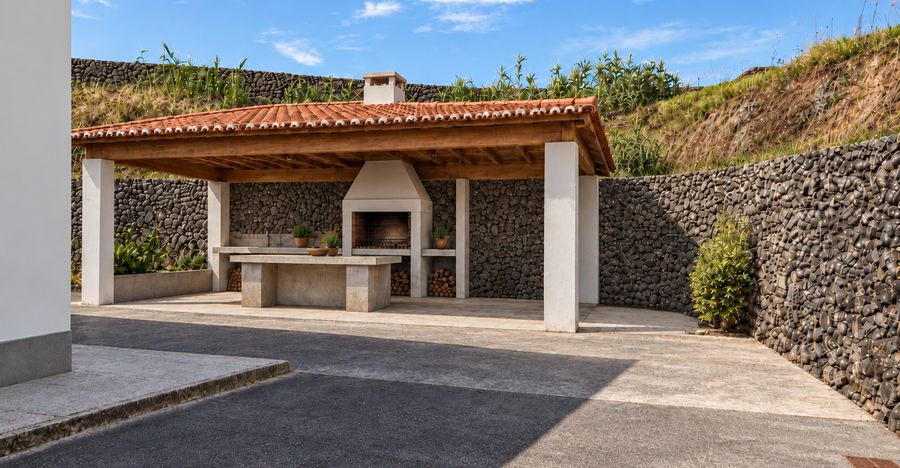Pátio exterior com churrasqueira coberta ao fundo, entre muros de pedra vulcânica
